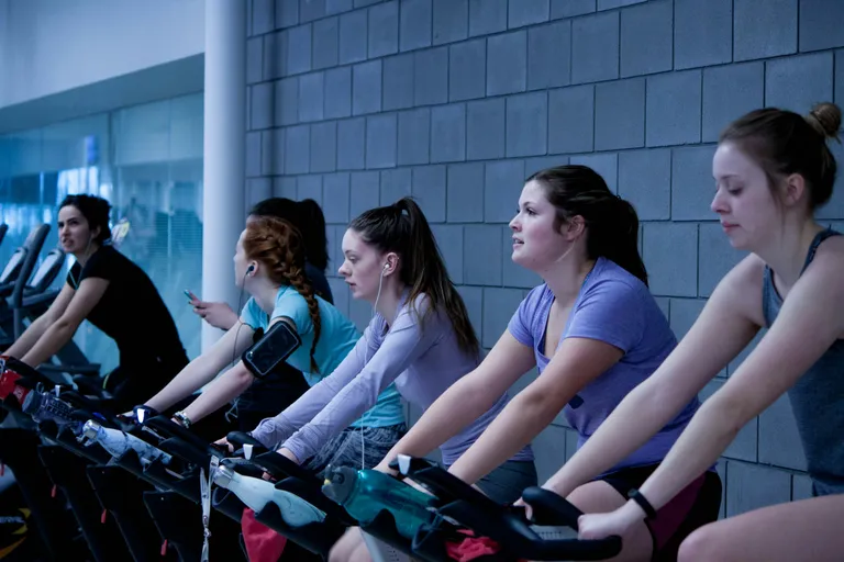 Alunas pedalando lado a lado numa aula de bike indoor