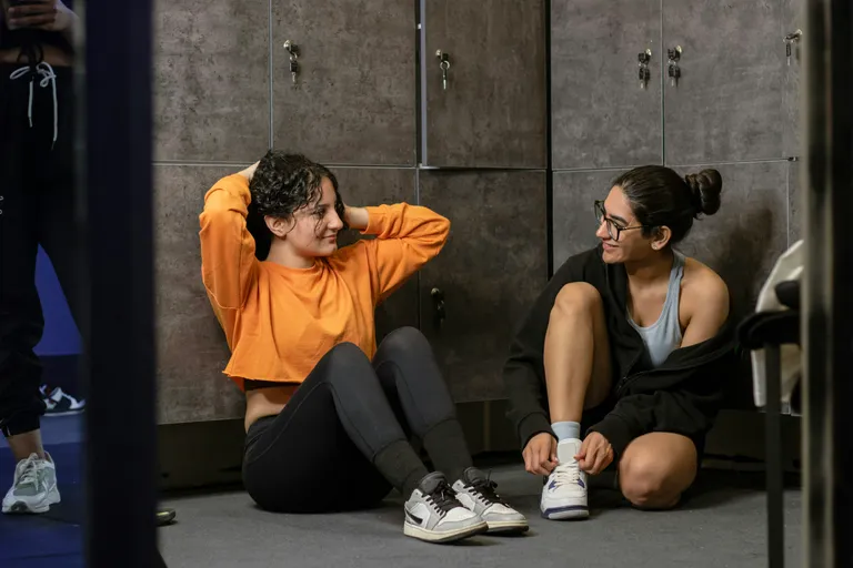 Duas alunas conversando sentadas no chão do vestiário da academia