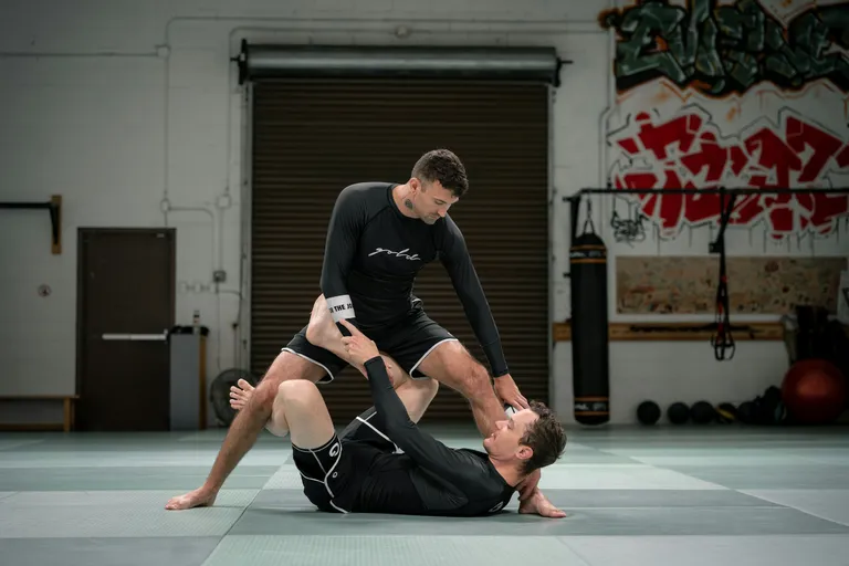 Professor de jiu-jitsu mostrando uma posição para o aluno no tatame