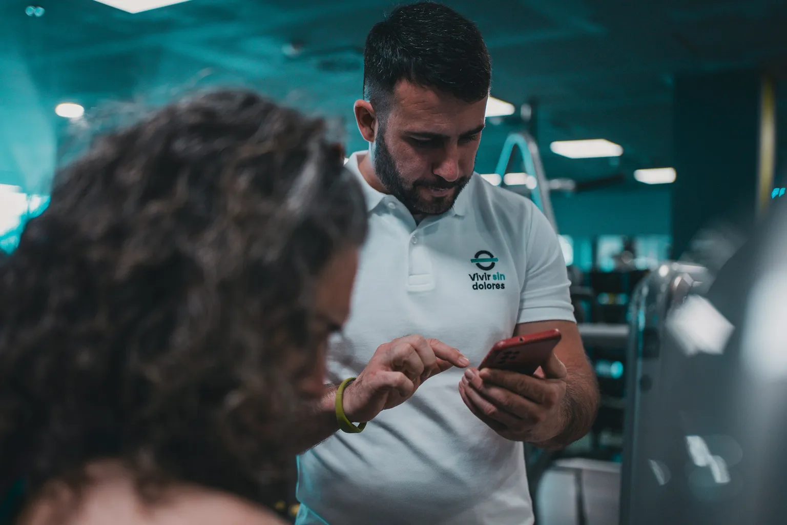 Professor de academia respondendo no celular ao lado de uma aluna